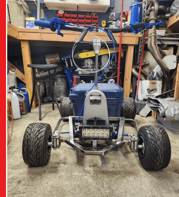 A blue and silver go kart sitting in front of a work bench.