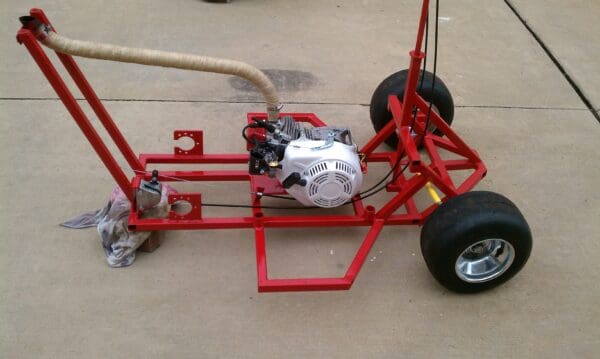 A red cart with a motor and wheels on the ground.